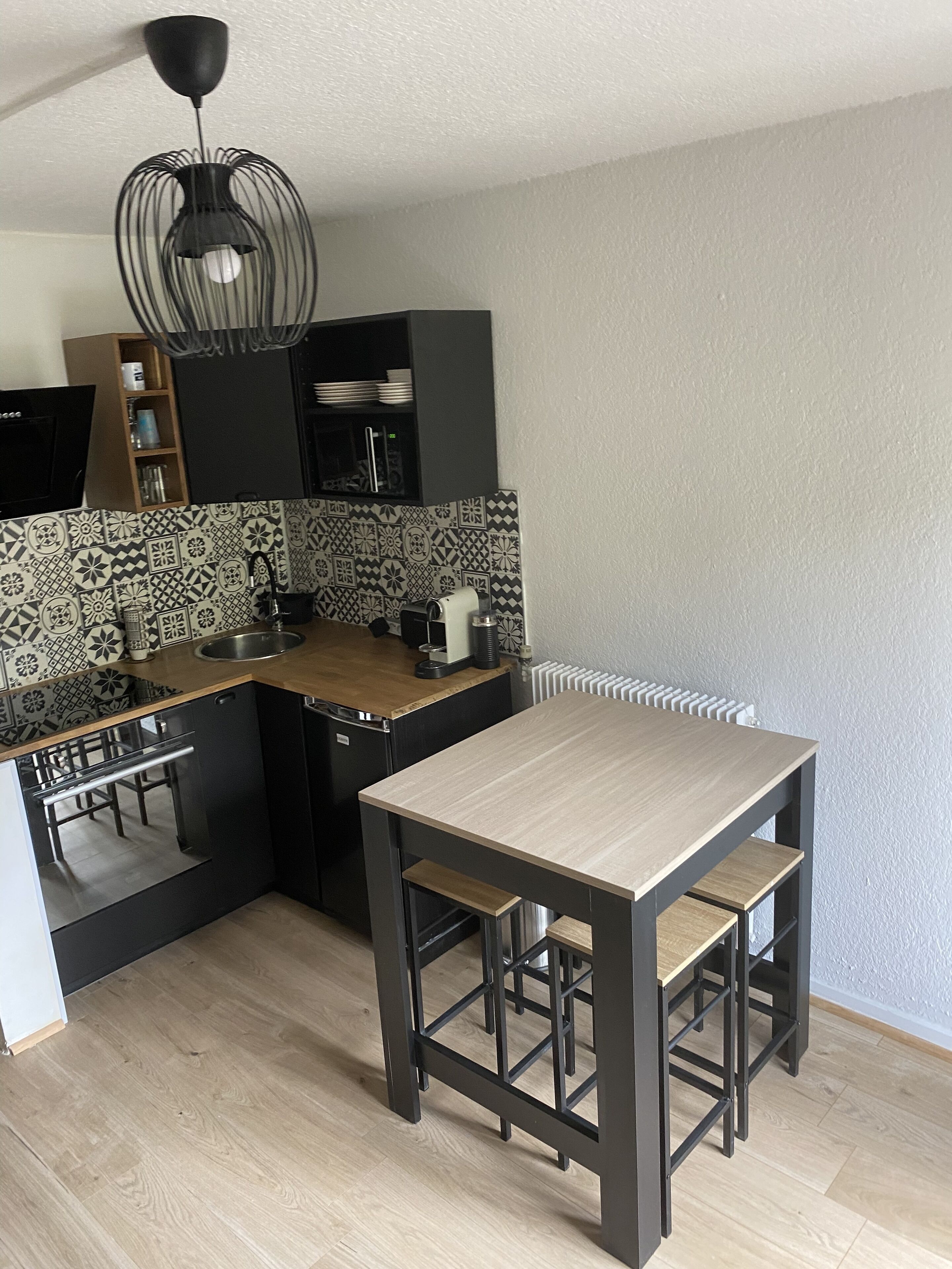 A compact kitchen with a wooden countertop, black cabinetry, a built-in dishwasher, and a black pendant light.