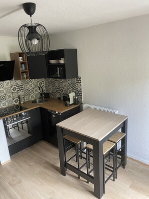 Una cocina compacta con encimera de madera, armarios negros, lavavajillas integrado y una lámpara colgante negra.