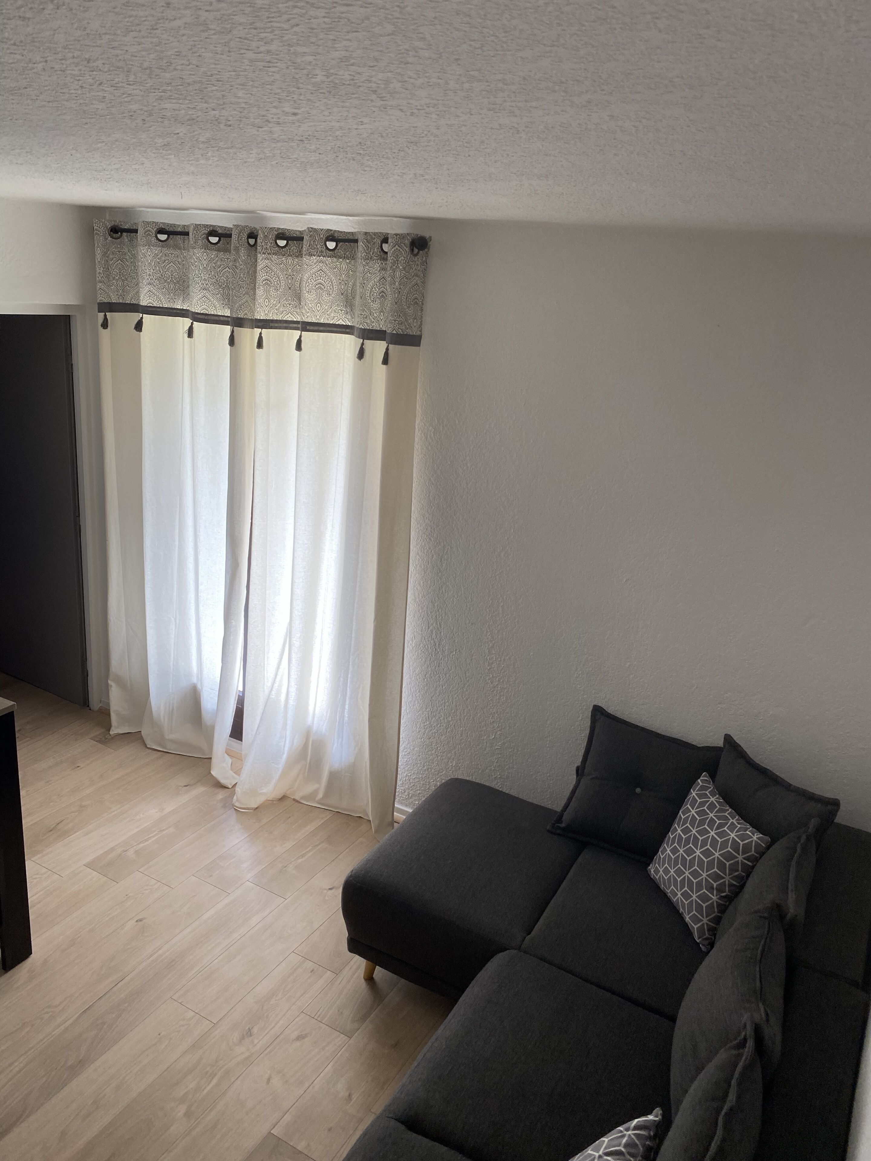 A modern living room with a grey sofa, a patterned curtain, and a wooden floor.