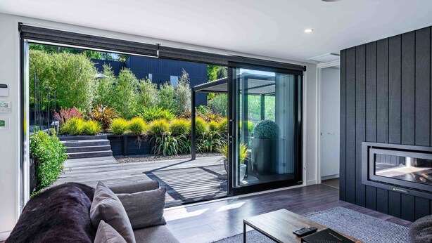 Una sala de estar moderna con un amplio ventanal corredero que da a un jardín, un televisor de pantalla plana montado en la pared y una zona de estar acogedora con una mesa de centro.