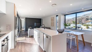 Una cocina moderna con una isla central, un comedor con mesa y sillas, y un amplio ventanal que ofrece vistas al exterior.