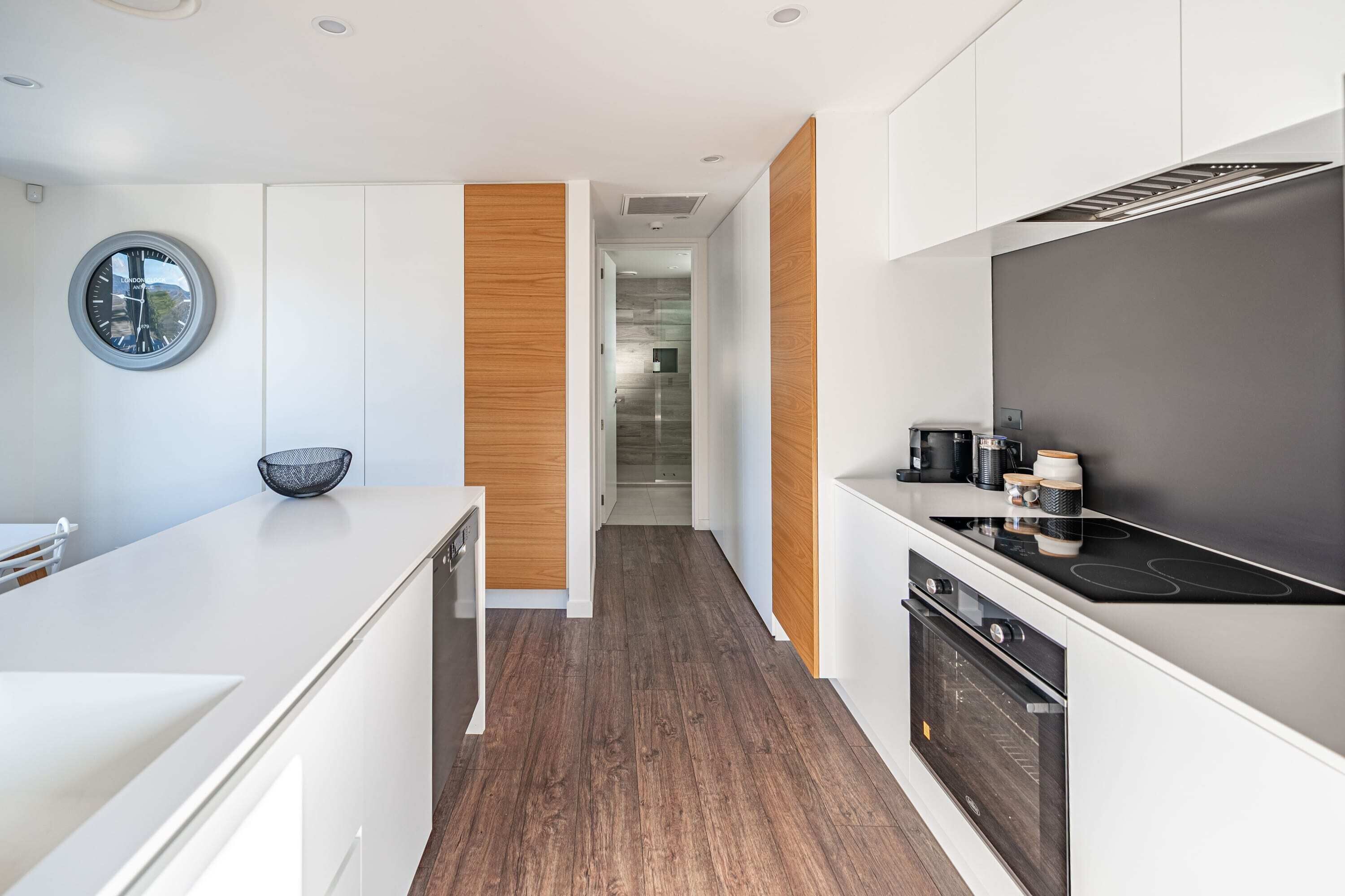 A modern kitchen with white cabinetry, a wooden accent wall, a round clock, and a black stove.