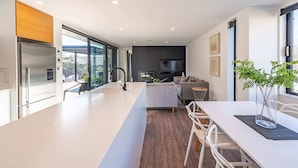 Una cocina moderna con una isla grande, un comedor con sillas blancas, un sofá y un televisor al fondo.