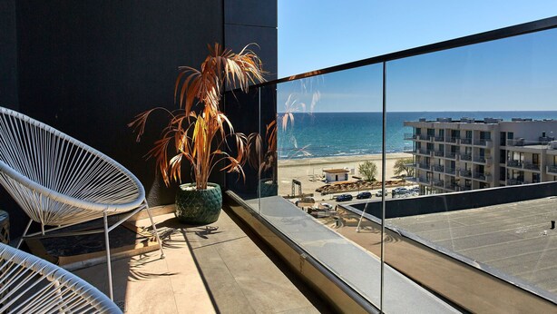 A balcony with a view of the beach and ocean, a potted plant, and a white chair. - Apartamente Stefan Resort 2 (Navodari)