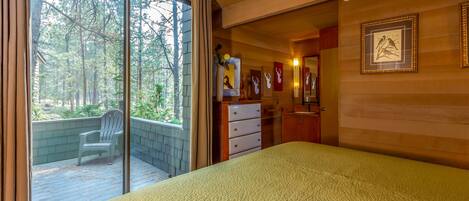 A bedroom with a large bed, a sliding glass door leading to a balcony, a dresser, and framed pictures on the wall.