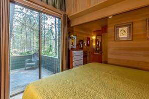 A bedroom with a large bed, a sliding glass door leading to a balcony, a dresser, and framed pictures on the wall.