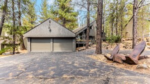 A modern house with a garage, surrounded by trees and a rocky landscape. - LEIS06 - Great for Families, Hot Tub, Ping Pong, Bunk Rooms (Sunriver)