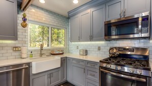 A modern kitchen with grey cabinets, stainless steel appliances, and a window with a view of trees. - LEIS06 - Great for Families, Hot Tub, Ping Pong, Bunk Rooms (Sunriver)