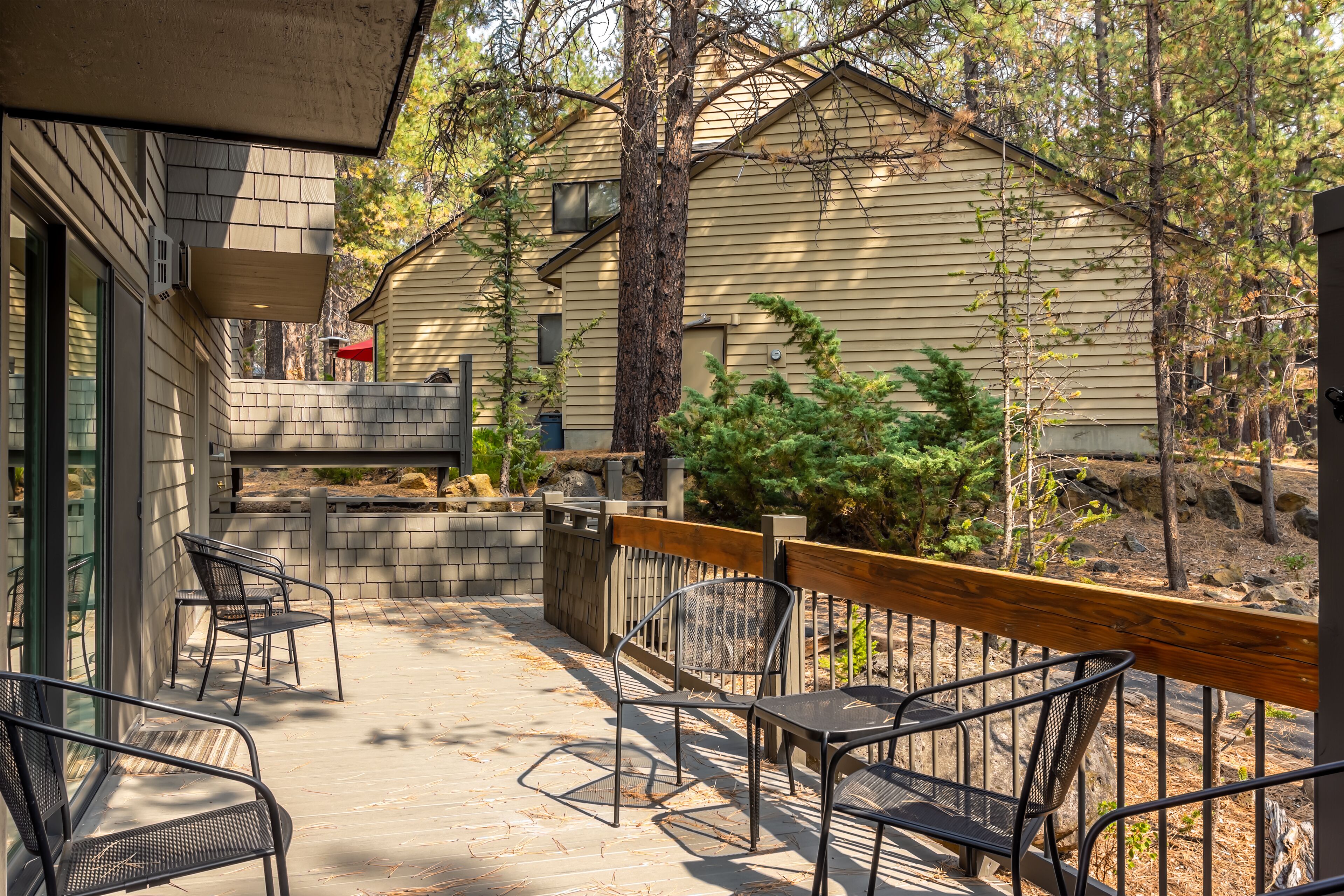 Une terrasse avec des sièges d’extérieur, une plateforme en bois et une vue sur une maison dotée d’un mur en pierre et d’un arbre.