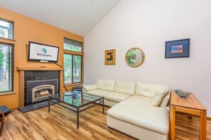 Un salon moderne avec une cheminée, un canapé, une table basse en verre et un téléviseur affichant le logo de Bennington Properties.