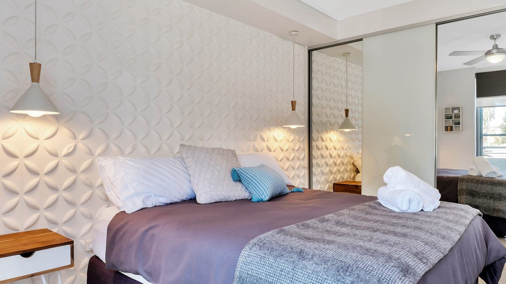 Een moderne slaapkamer met een bed, kussens, een nachtkastje en een bijzettafeltje.