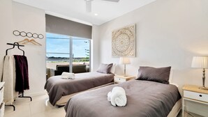 Habitación de hotel con dos camas, un ventanal con vistas, una obra de arte colgada en la pared y una mesita de noche con lámpara.