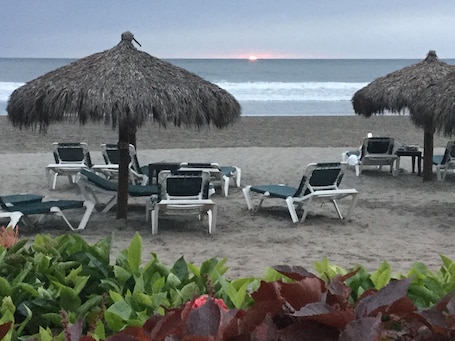 A beach with lounge chairs and thatched umbrellas.