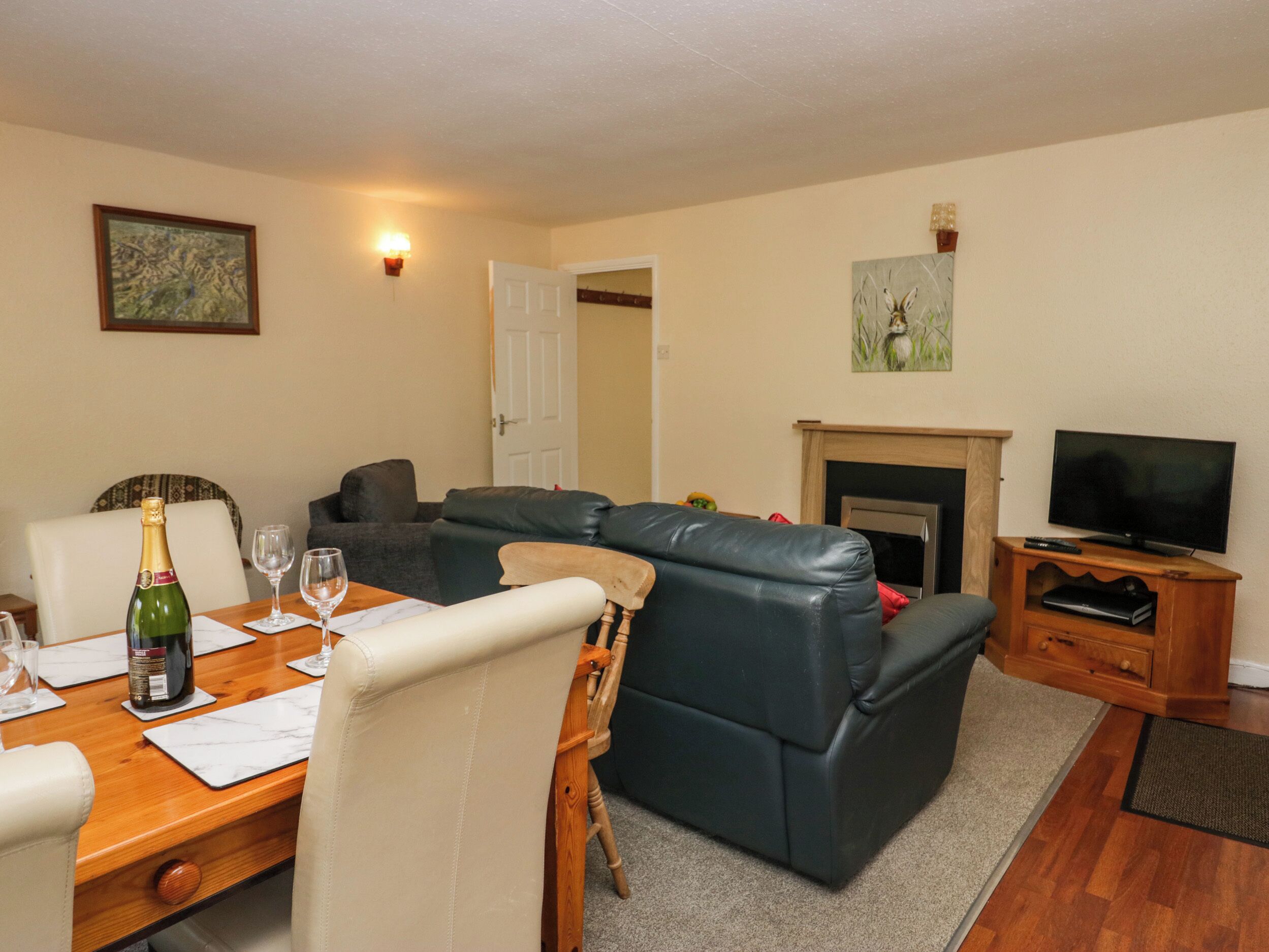 A living room with a dining table, leather sofa, television, fireplace, and artwork on the walls.
