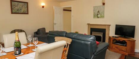 A living room with a dining table, leather sofa, television, fireplace, and artwork on the walls.