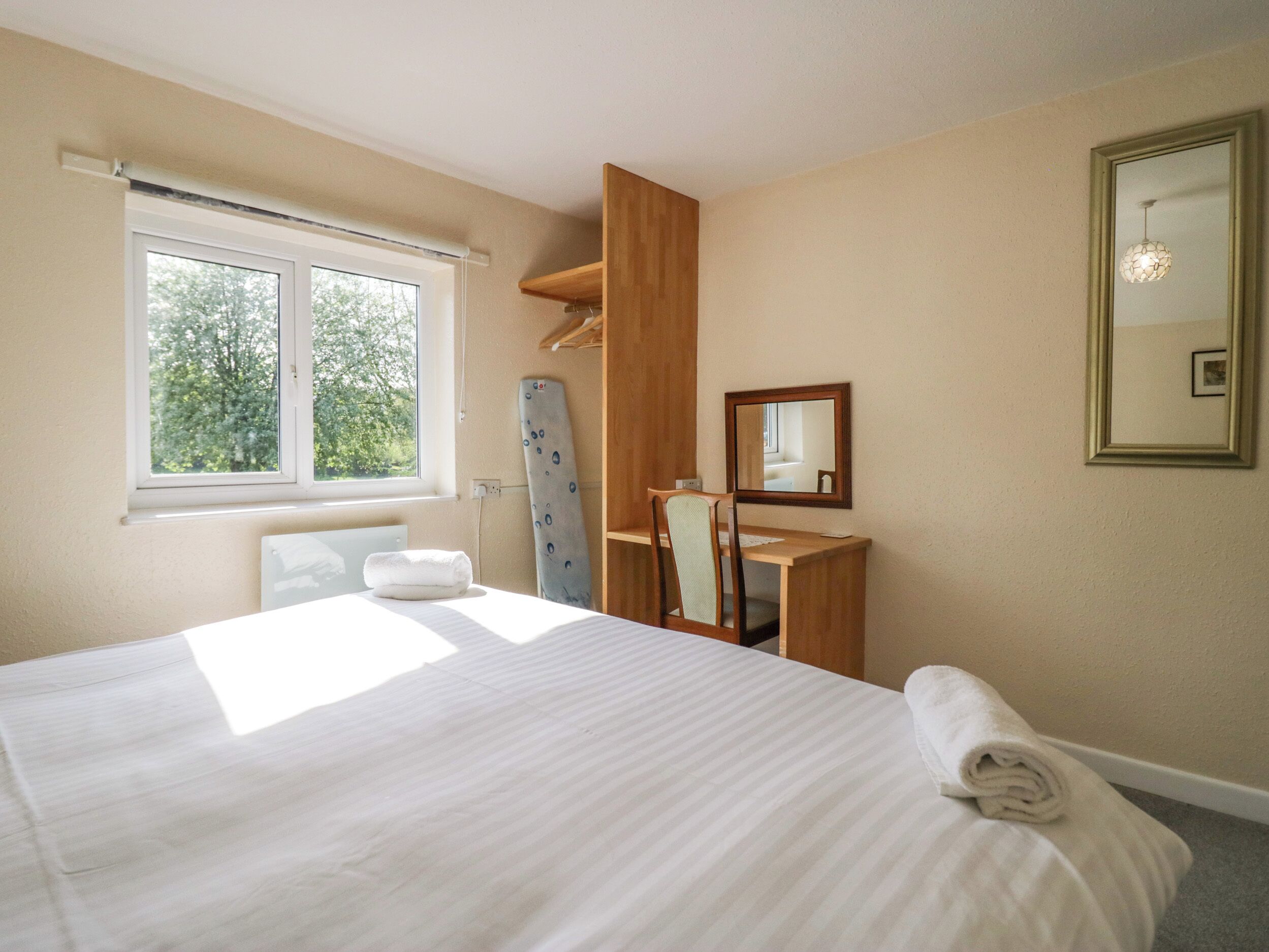A bedroom with a bed, a desk, a chair, a mirror, and a window.