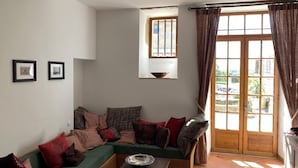 Ein gemütliches Wohnzimmer mit einem grünen Sofa, gemusterten Kissen, einem Holztisch und einem Fenster mit Vorhängen.