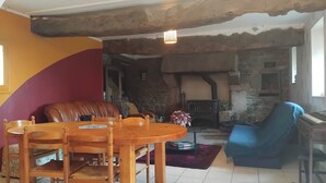 A cozy living room with a stone fireplace, a dining table with chairs, a blue armchair, and a leather sofa. - Charmant Gîte 6 à 10 Personnes en Bord de mer (Lannion)