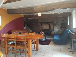 Un salon chaleureux avec une cheminée en pierre, une table à manger avec des chaises, un fauteuil bleu et un canapé en cuir.