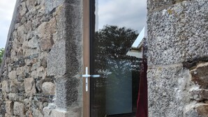A stone building with a glass door, wooden flooring, and a visible cat. - Charmant Gîte 6 à 10 Personnes en Bord de mer (Lannion)