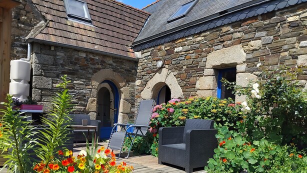 A stone building with a wooden deck, outdoor seating, and flower beds. - Charmant Gîte 6 à 10 Personnes en Bord de mer (Lannion)