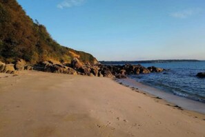 Une plage bordée d’une côte rocheuse, sous un ciel dégagé.