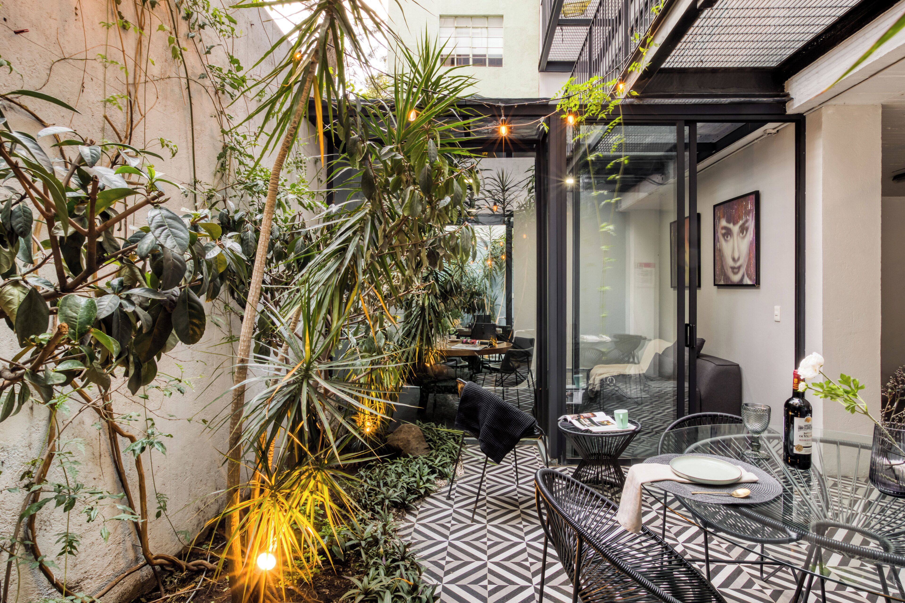 A modern outdoor patio with geometric patterned flooring, black metal furniture, and lush greenery.