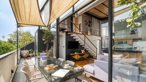 A modern interior with a glass dining table, white chairs, a sofa, and a staircase leading to an upper level. - ULIV Parque México (Mexico City)