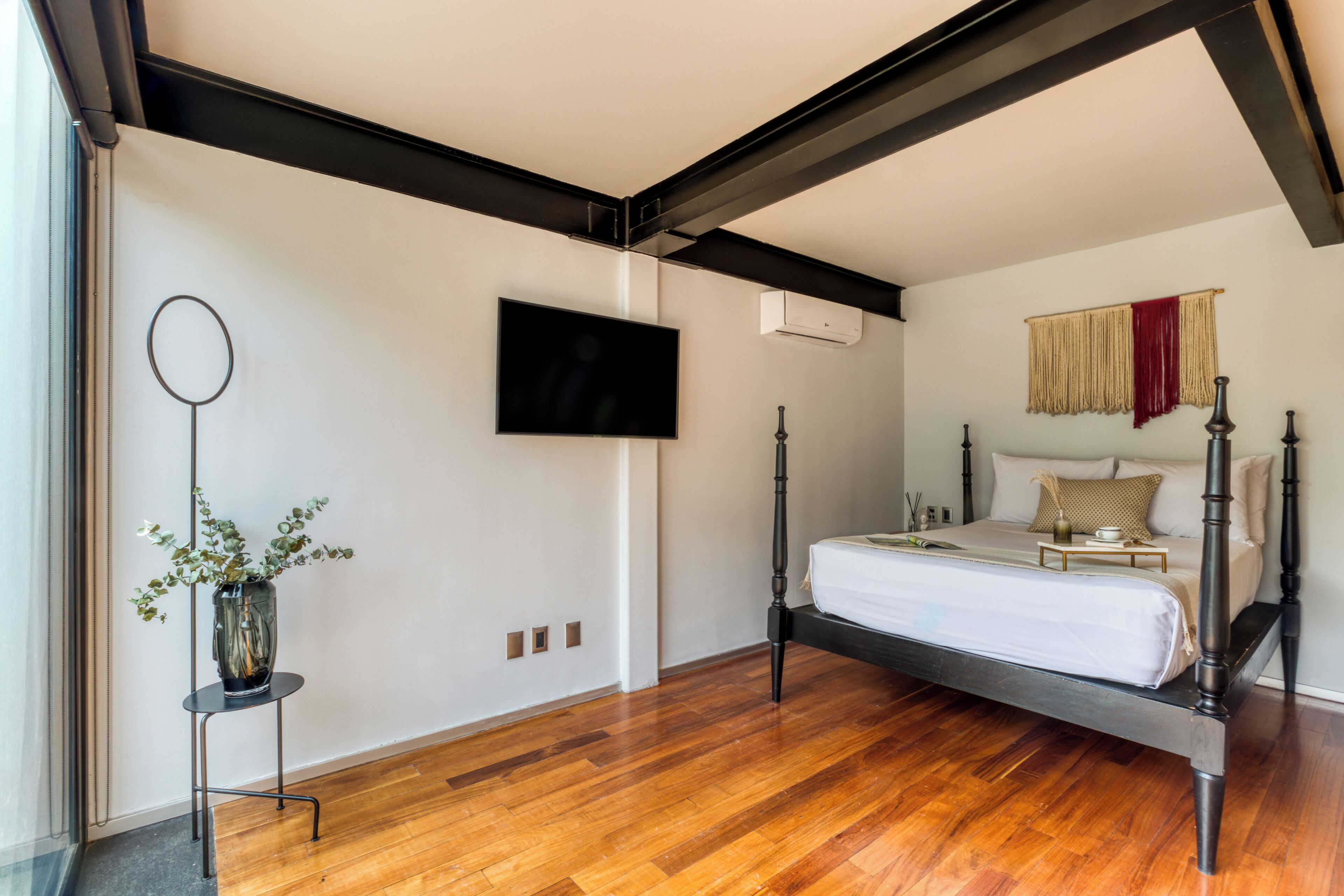 Un dormitorio con cama, televisor montado en la pared y ventana.