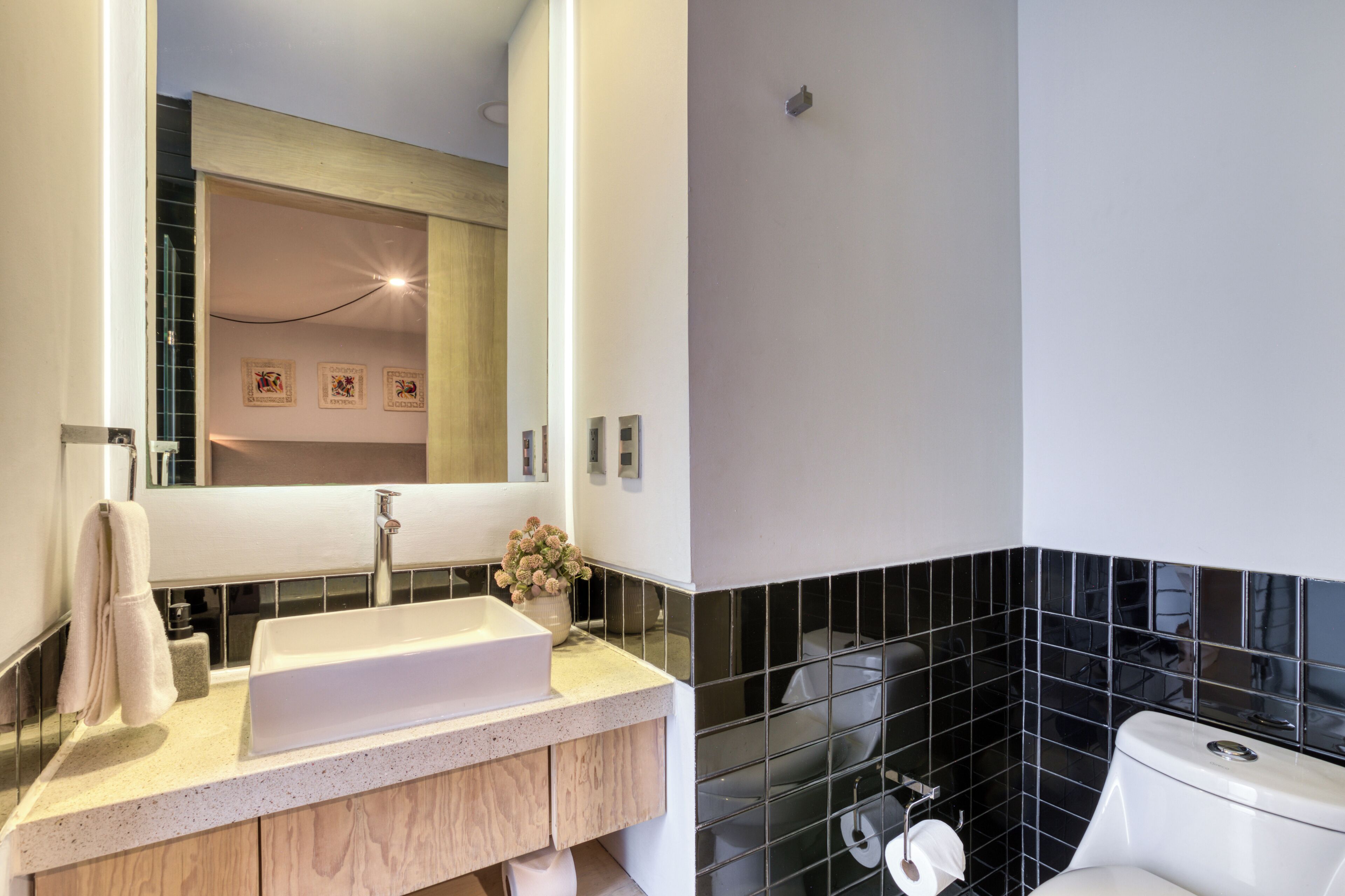 Ein modernes Badezimmer mit einem weißen Waschbecken, einem Spiegel und schwarzen Fliesenwänden.