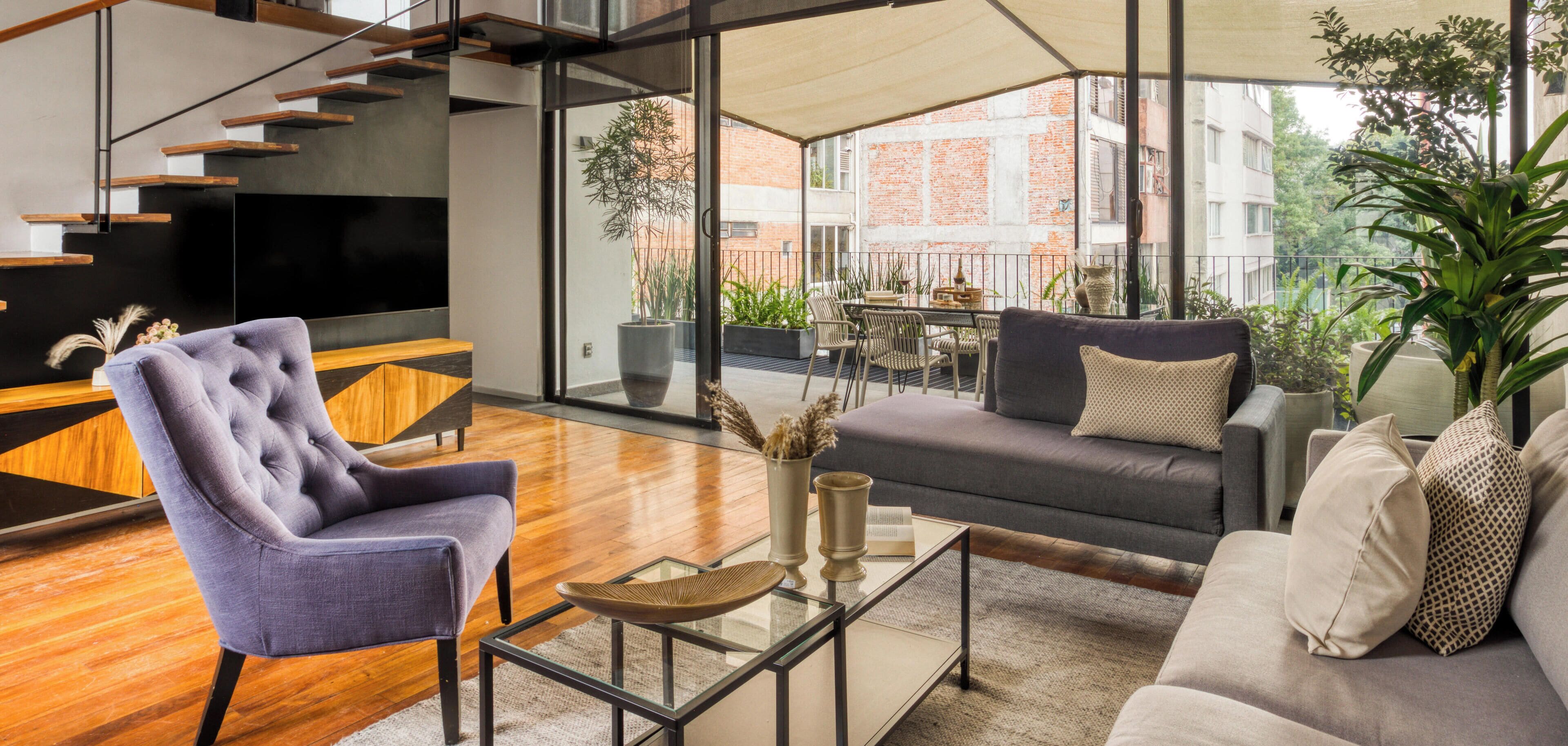 A modern living room with a sofa, armchair, and coffee table. A staircase is visible in the background.