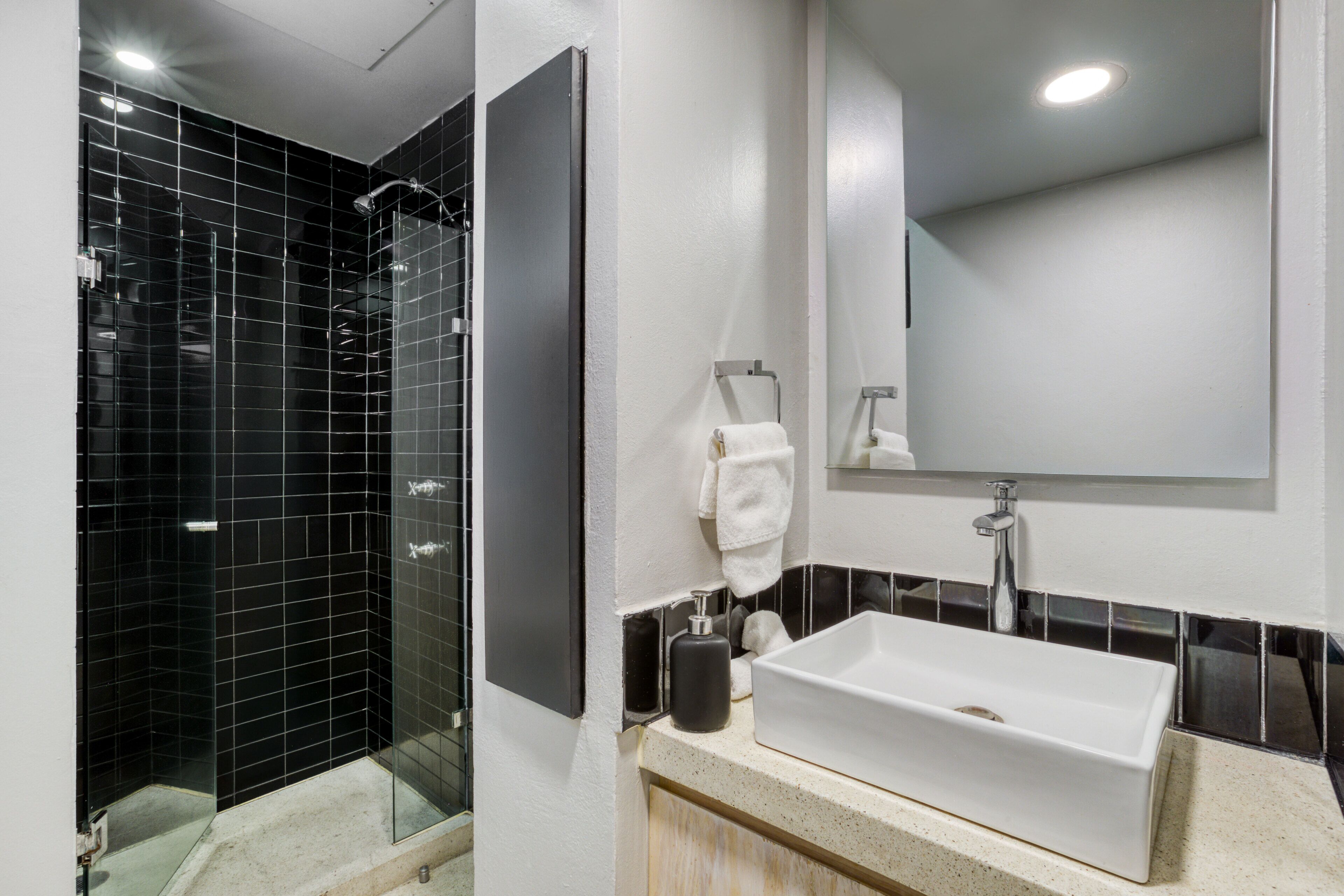 Une salle de bain moderne avec une douche carrelée de noir, un lavabo blanc et un miroir au-dessus.