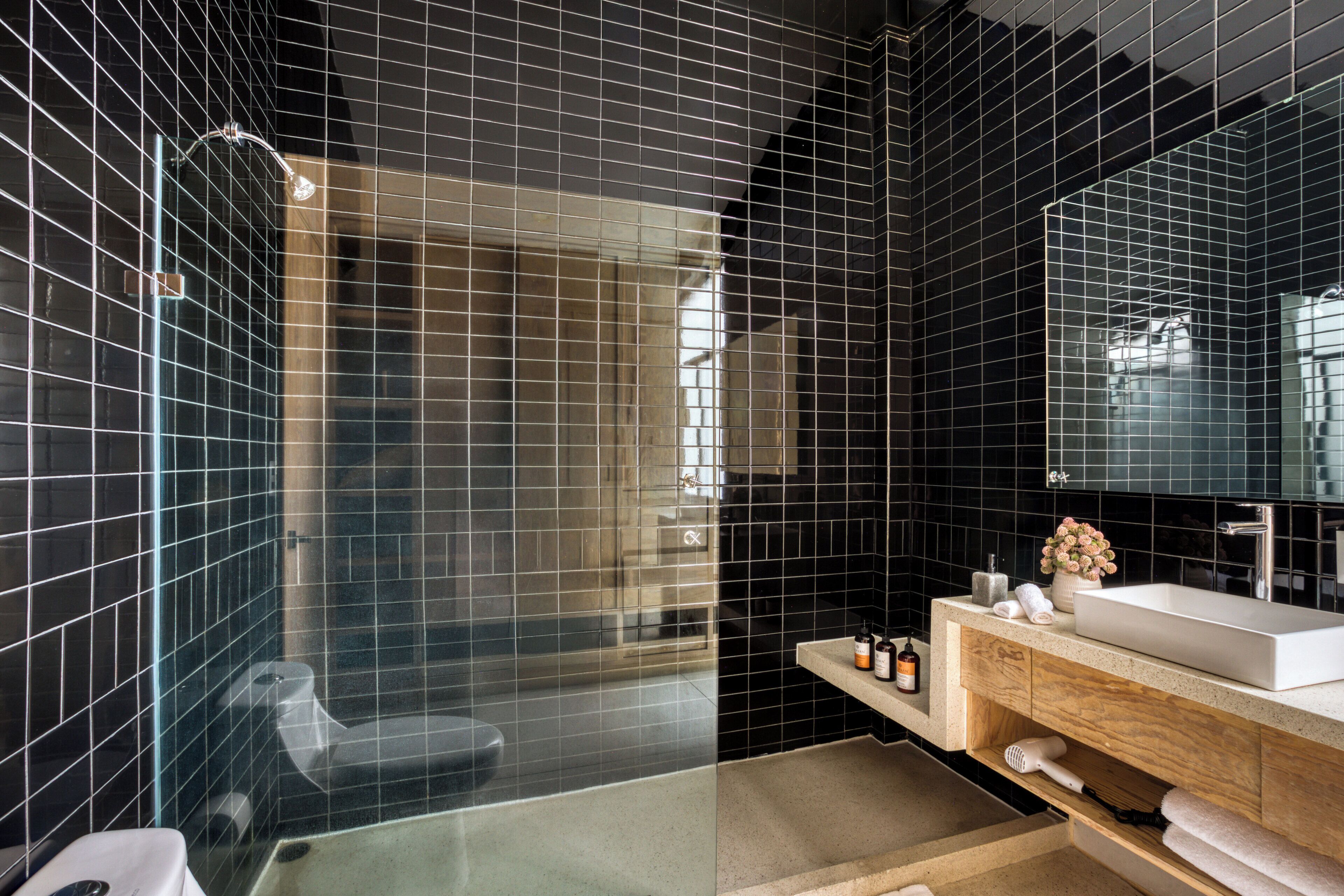 A modern bathroom with black tiles, a glass shower enclosure, a wooden vanity, and a large mirror.