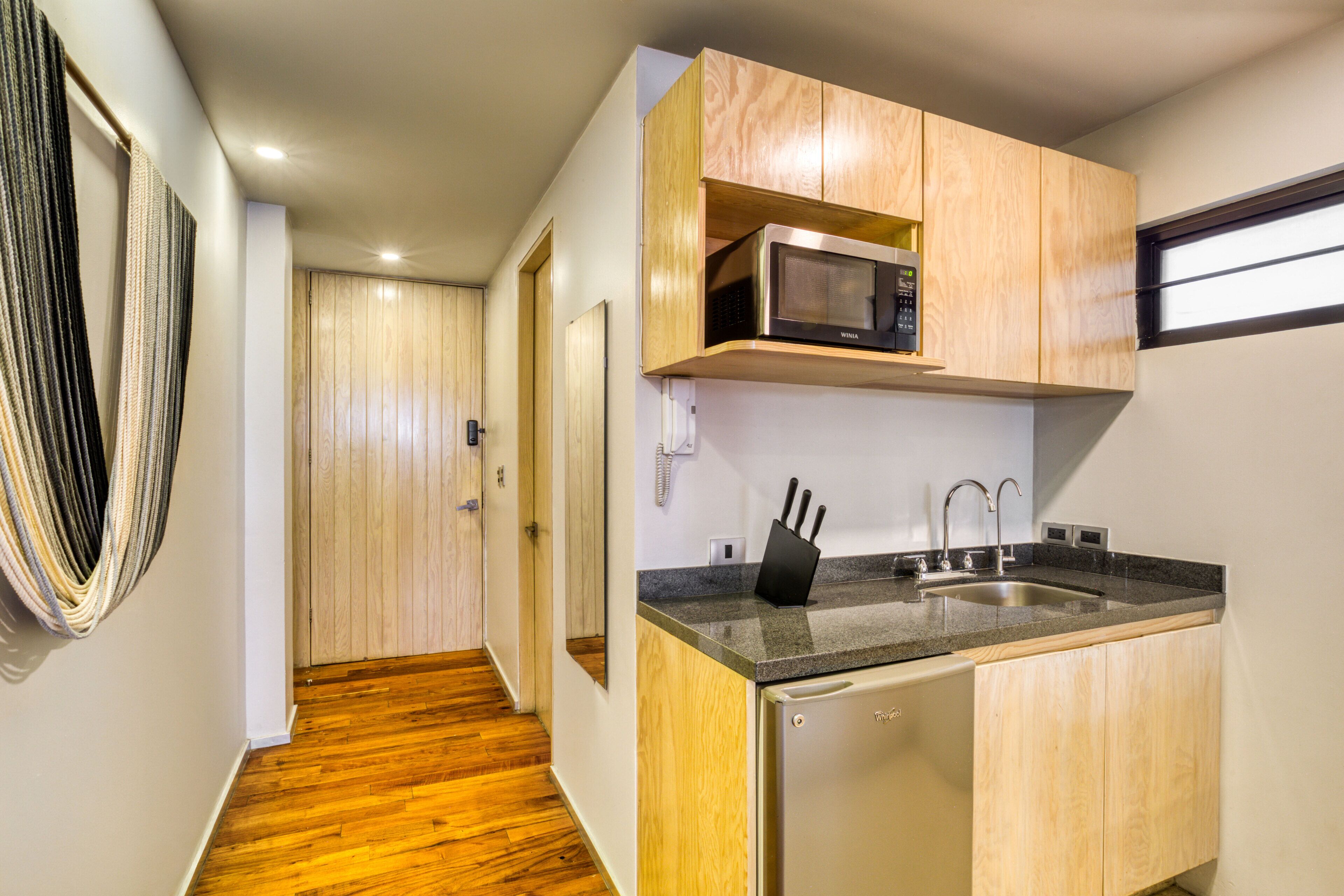 A compact kitchen with wooden cabinets, a built-in microwave, a sink, and a knife block.