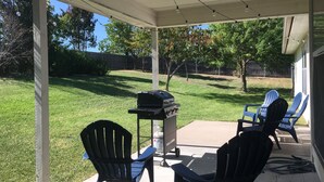 A covered patio with a grill, two Adirondack chairs, and a table. - Perfect home for Baylor, Silos, and Business guests (Hewitt)