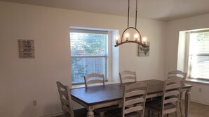 A dining room with a wooden table and six chairs, a chandelier, and a window with blinds. - Perfect home for Baylor, Silos, and Business guests (Hewitt)