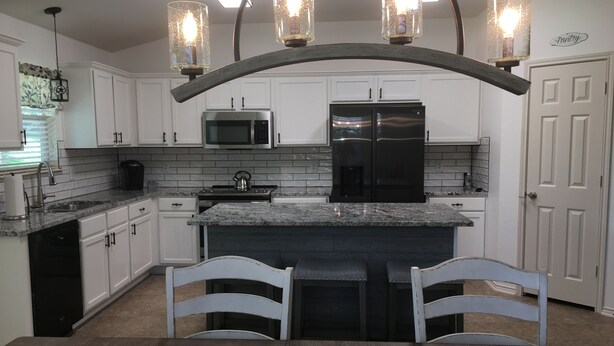 A modern kitchen with white cabinets, a black refrigerator, a microwave, and a granite countertop. There are two bar stools and a dining table. - Perfect home for Baylor, Silos, and Business guests (Hewitt)