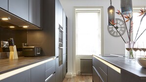 A modern kitchen with dark cabinetry, a wooden countertop, a built-in oven, and a window with blinds. - 11 Redcliffe Parade (Bristol)