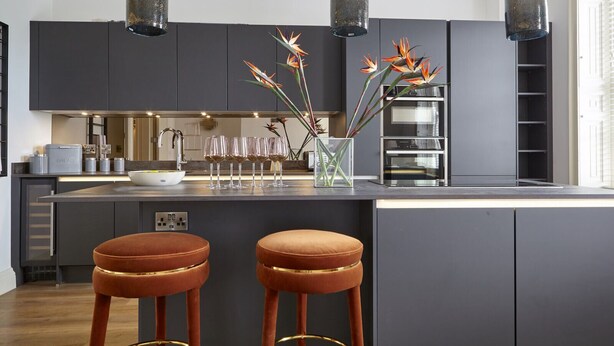 A modern kitchen with dark cabinetry, a central island with stools, and pendant lighting. - 11 Redcliffe Parade (Bristol)
