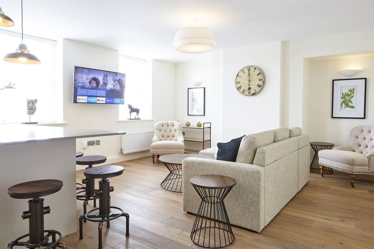 Uma sala de estar moderna com um sofá, poltronas, uma mesa de centro e uma TV fixada na parede.