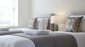 A hotel room with two beds, a window with blinds, a wall-mounted lamp, and a view of buildings outside. - 11 Redcliffe Parade (Bristol)