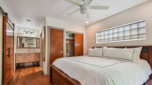 Een slaapkamer met een houten bed, een plafondventilator, een inloopkast en een groot raam.