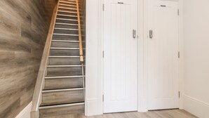A staircase with a wooden finish, white double doors with a keypad lock, and a light-colored wooden floor. - The Stannary (Helston)