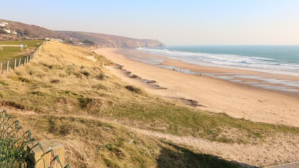 A coastal landscape with a sandy beach, grassy dunes, and a clear sky. - The Stannary (Helston)