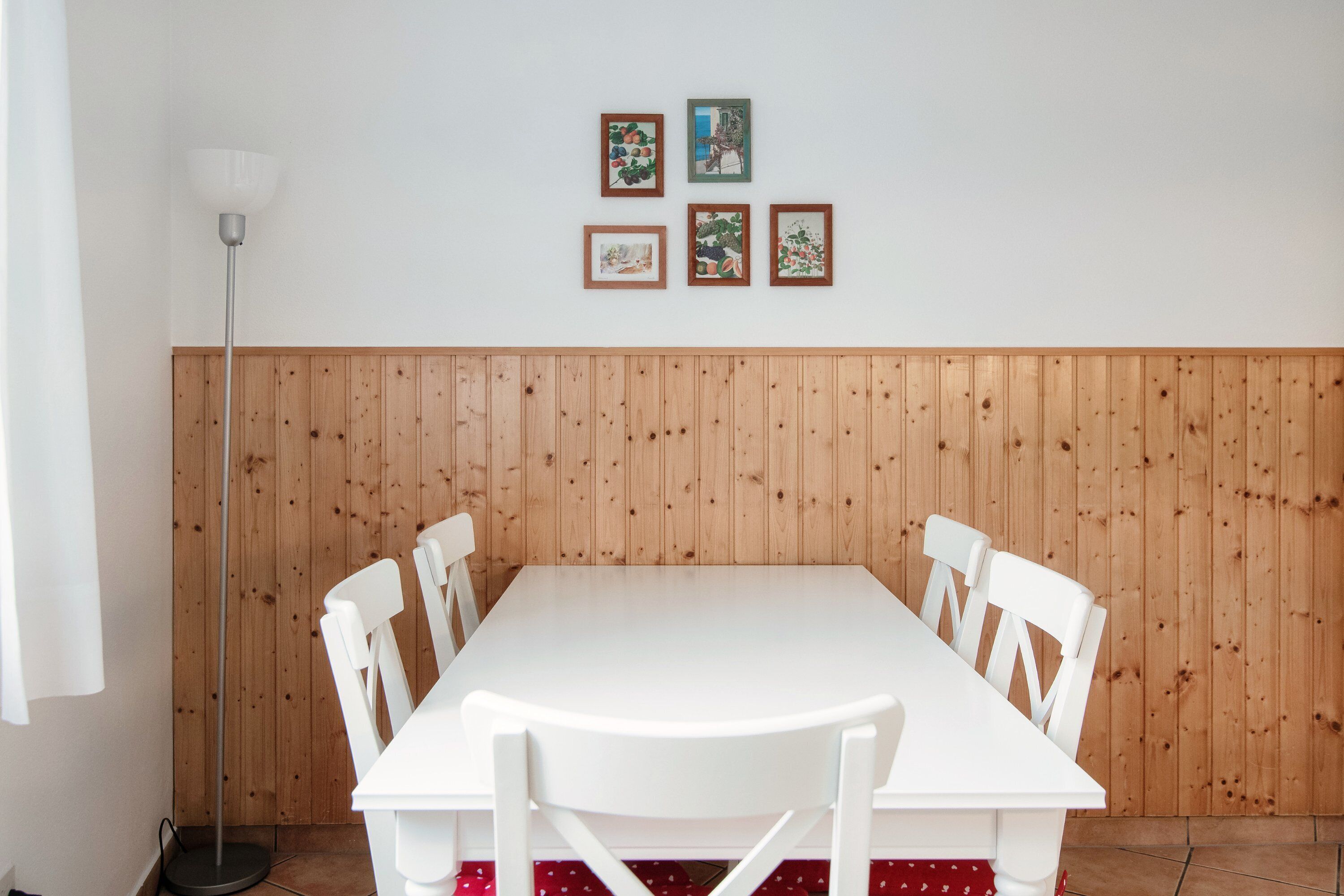 Ein Essbereich mit einem weißen Tisch und Stühlen, Holzvertäfelung an der Wand und vier gerahmten Bildern.