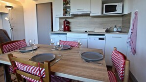 Un comedor con una mesa de madera dispuesta para cuatro, sillas a rayas rojas y blancas, un microondas y una cafetera en la zona de la cocina.