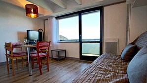 Habitación de hotel con una cama, un escritorio con computadora, dos sillas, una mesita y un ventanal con vistas.
