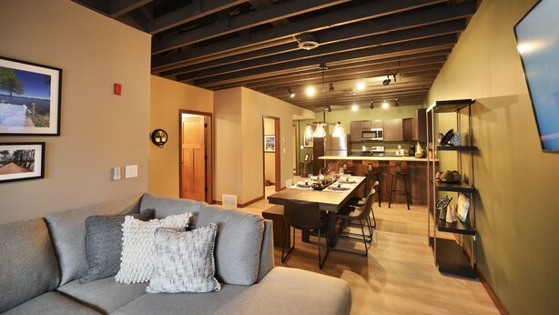 A modern living room with a sofa, dining table, and kitchen area. - Modern Rustic 2BR Condo in Downtown Minocqua—Walk to Shops, Dining & Lake (Minocqua)