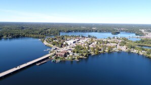 An aerial view of a lakeside town with a bridge, docks, and residential buildings. - Modern Rustic 2BR Condo in Downtown Minocqua—Walk to Shops, Dining & Lake (Minocqua)