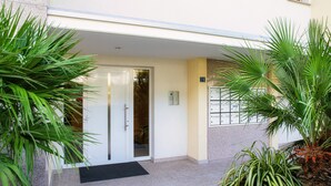 Entrada de hotel con puerta, felpudo negro y plantas en macetas.